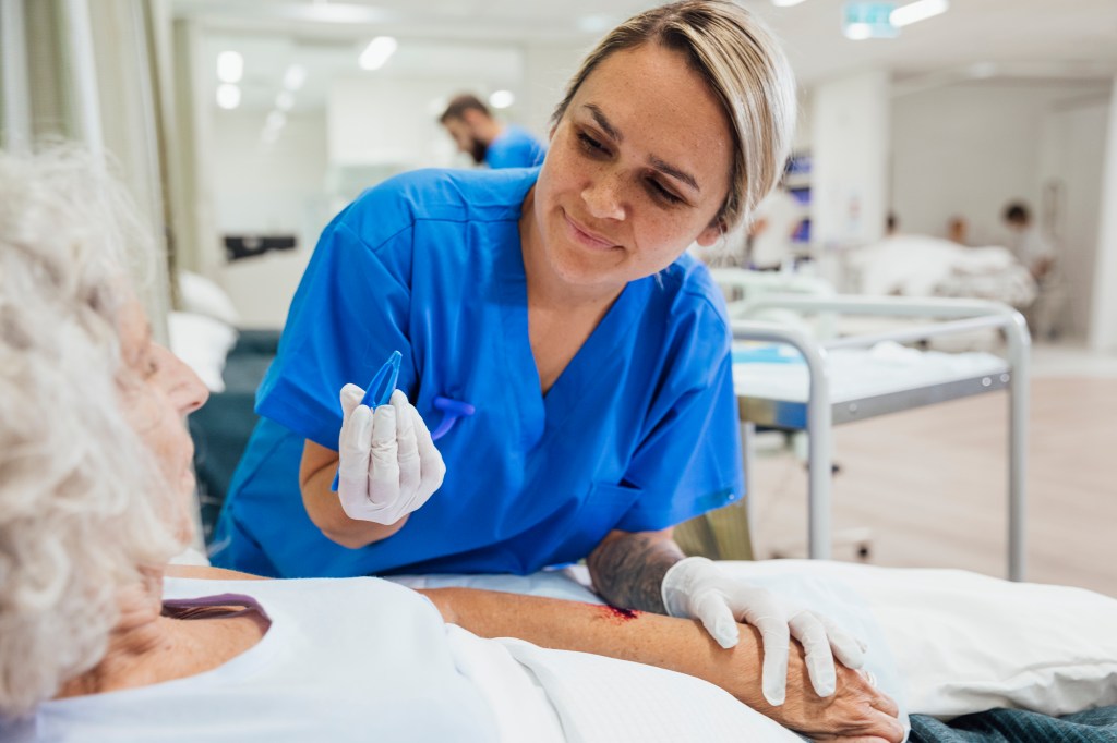 A shot of a young nurse cleaning a senior woman's wound on the hospital ward.
